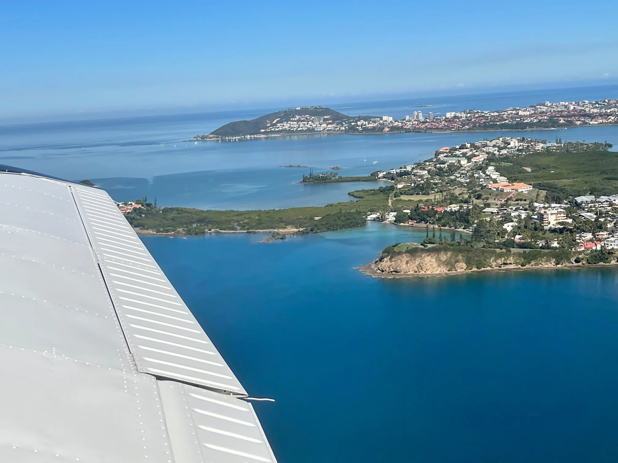 Vue de l'aile d'un avion au décollage de Magenta au-dessus de la baie et de la presqu'île de Nouméa
