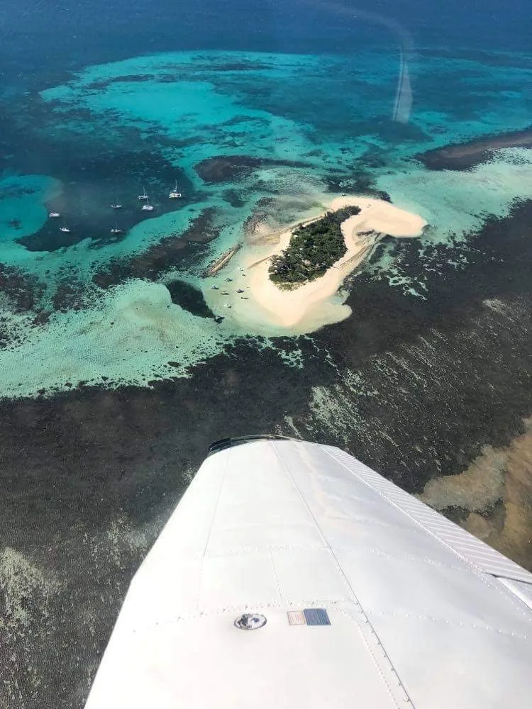 Vue aérienne de l'îlot Larégnère, banc de sable et récif corallien turquoise avec voiliers au mouillage